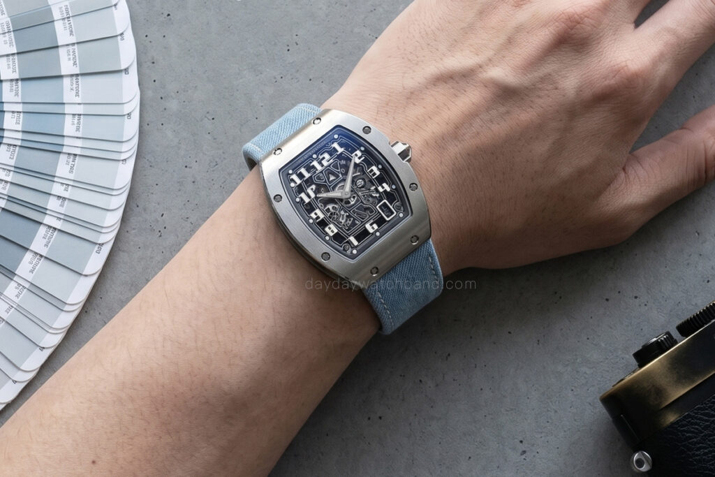 Wrist shot of Richard Mille RM 67-01 fitted with blue denim watch strap by Daydaywatchband, lifestyle POV with Pantone color fan and camera on grey concrete background