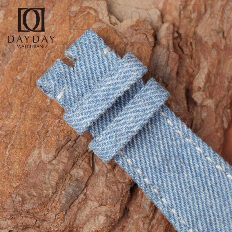 Macro close-up of the buckle end of a denim canvas watch strap showing punch holes, keeper loop and tight denim weave texture
