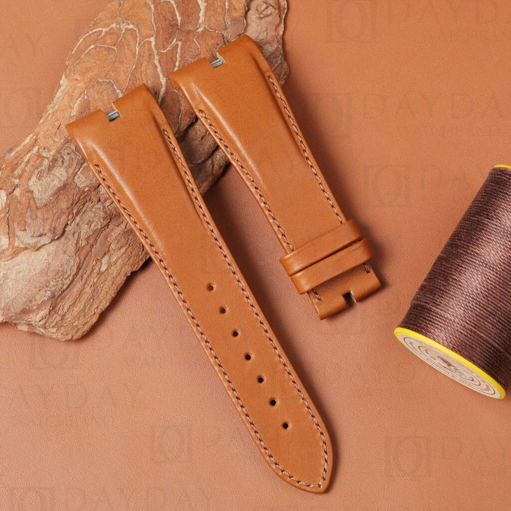 Personalized leather watch band for Roger Dubuis Excalibur in cognac calfskin – angled view showing lug ends, strap body, and keeper against stone prop